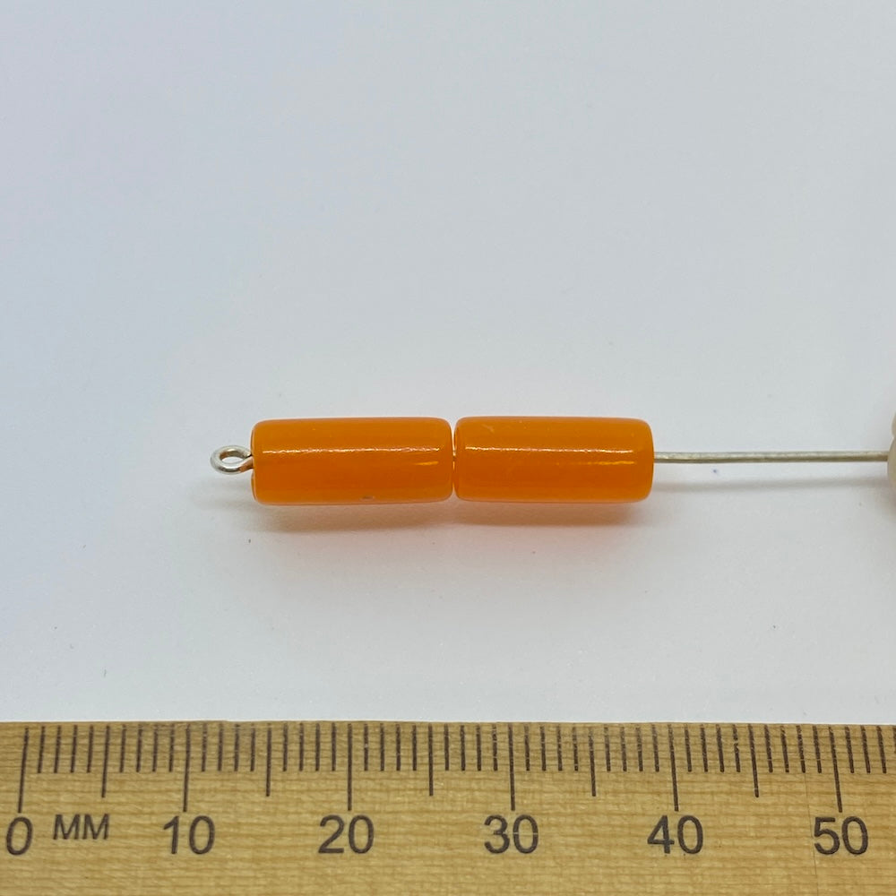 A pair of vibrant coloured tube beads against a ruler for size on a white background for the purposes of making craft and jewelry