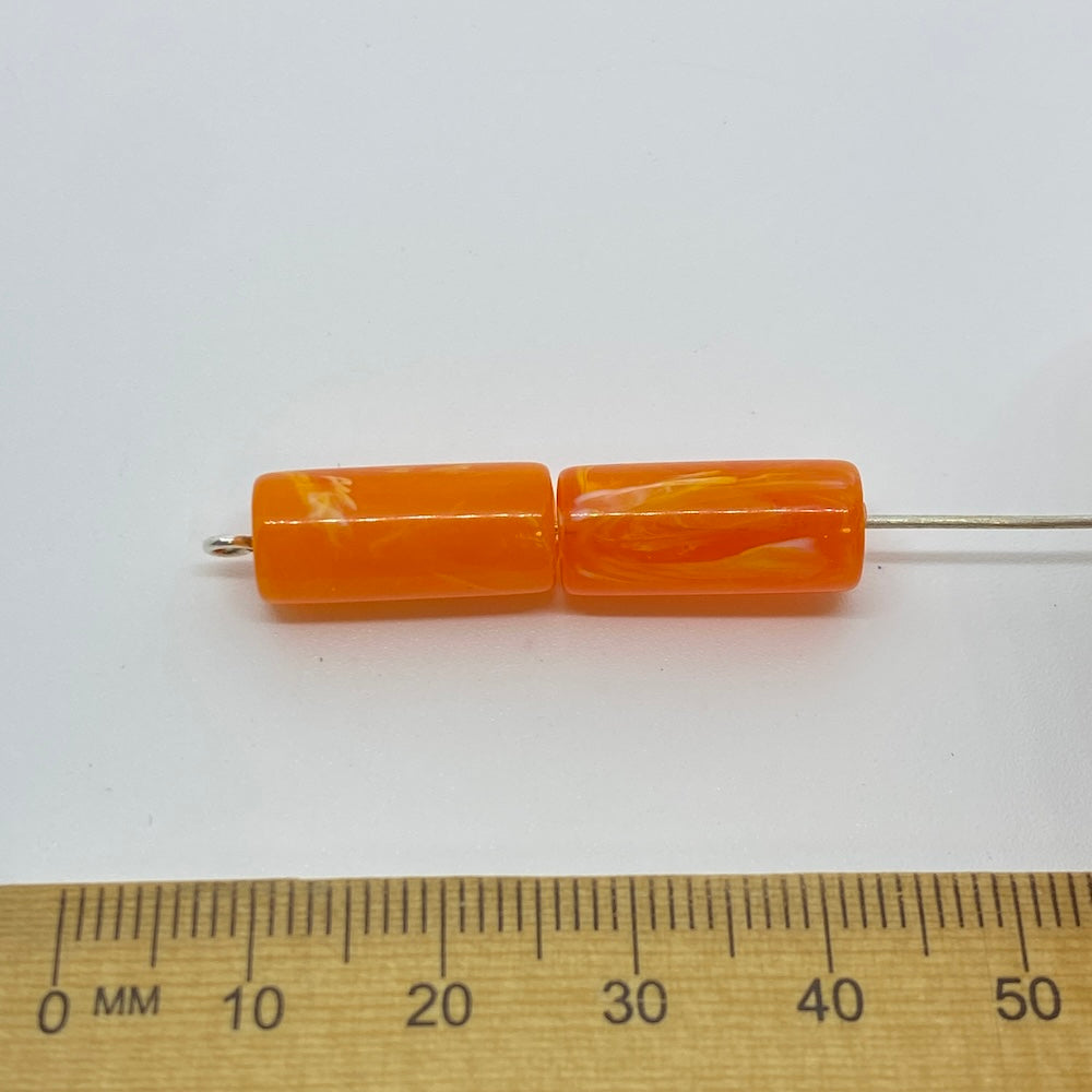 A pair of vibrant coloured tube beads against a ruler for size on a white background for the purposes of making craft and jewelry