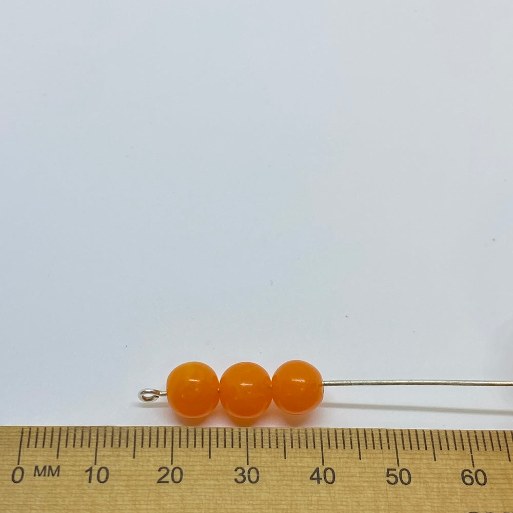 Three vibrant coloured round beads against a ruler for size on a white background for the purposes of making craft and jewelry