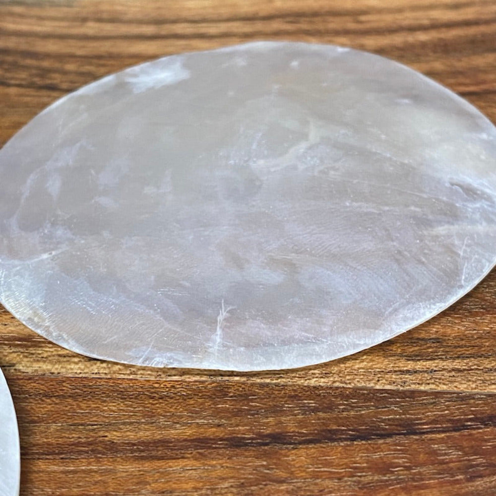 white, round capiz shell disc placed on a wooden surface used for wedding name place settings, bonbonniere, artwork and craft items displayed on a wooden surface