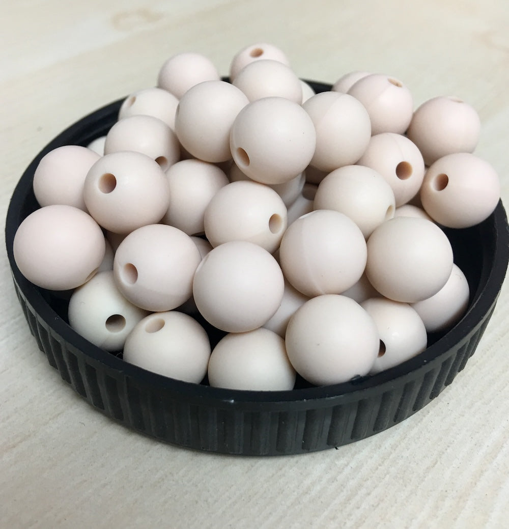 A black container filled with blush pink round silicone beads, with a threading hole visible on each bead.