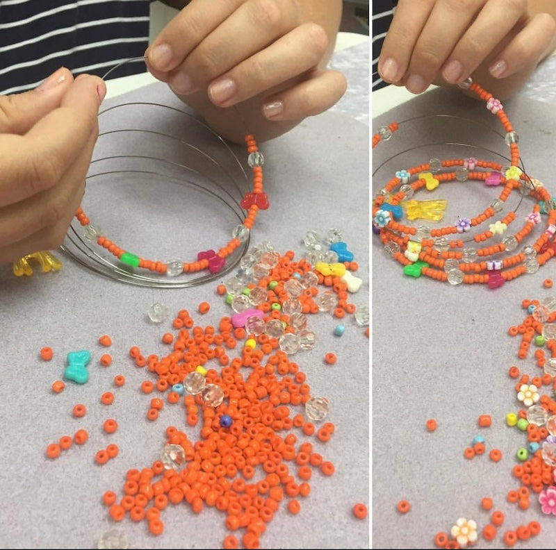 Child making a beaded hanging decoration on a grey textured surface using orange beads and colourful focal beads
