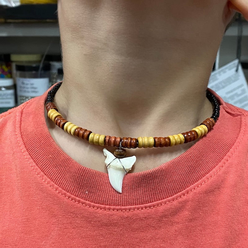Sample of a wood and shark tooth necklace being worn by a boy in a rust brown t-shirt