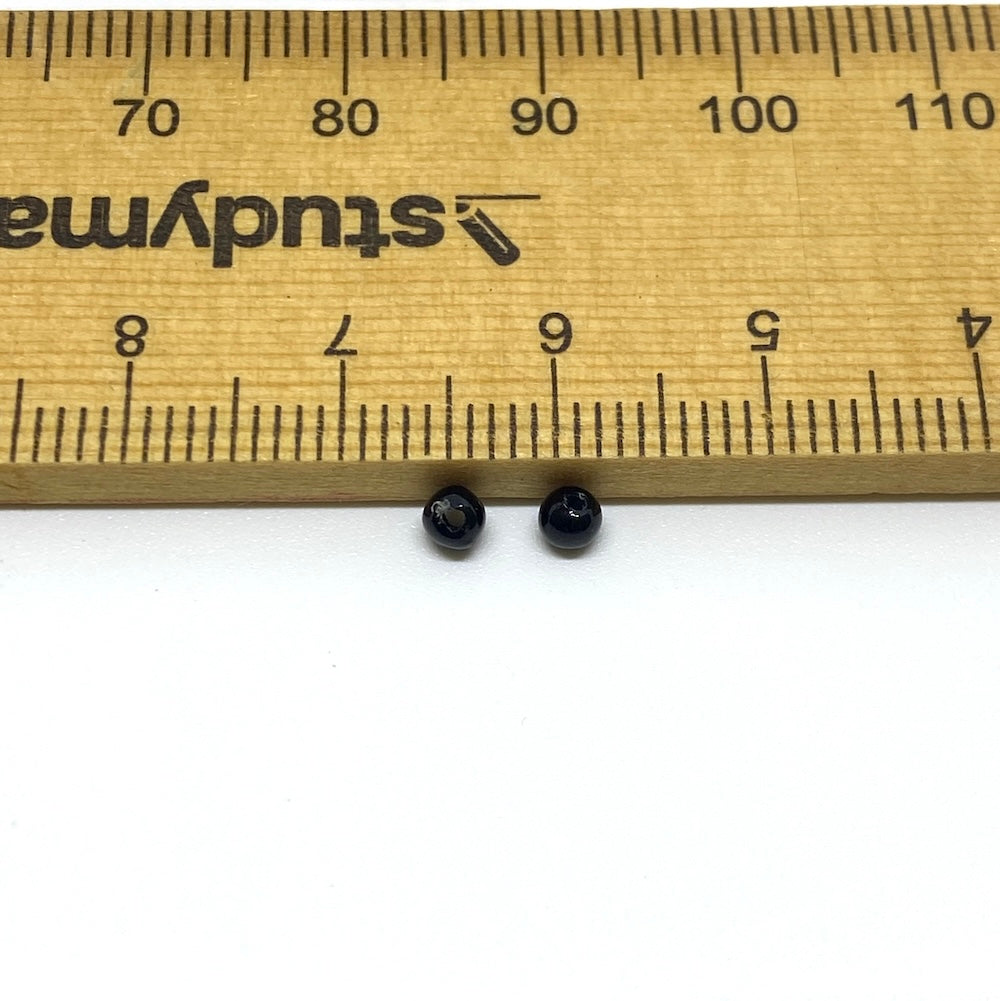 Two black beads next to a ruler for size reference on a white background