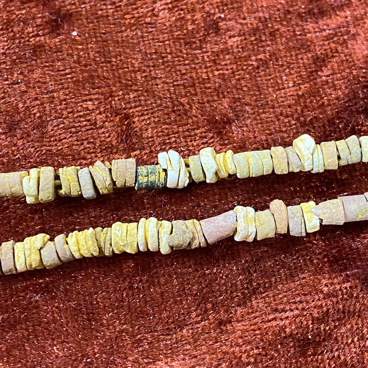A close up of colored desert sand color faience beads arranged in lines, with varying shapes and textures.