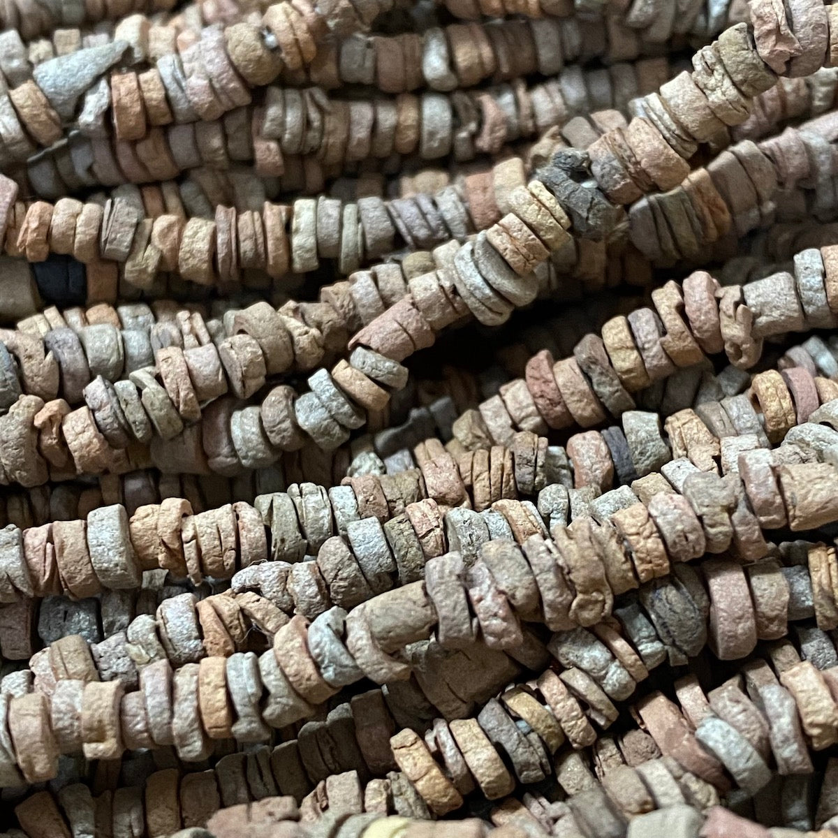 A collection of brown terracotta-colored vintage faience beads arranged in lines, with varying shapes and textures.