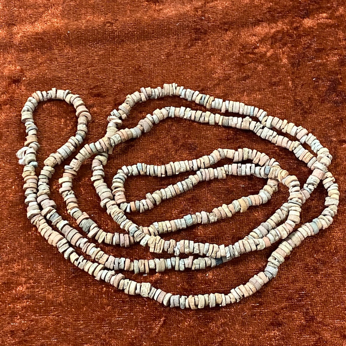 A collection of brown terracotta-colored vintage faience beads arranged in loops, with varying shapes and textures.