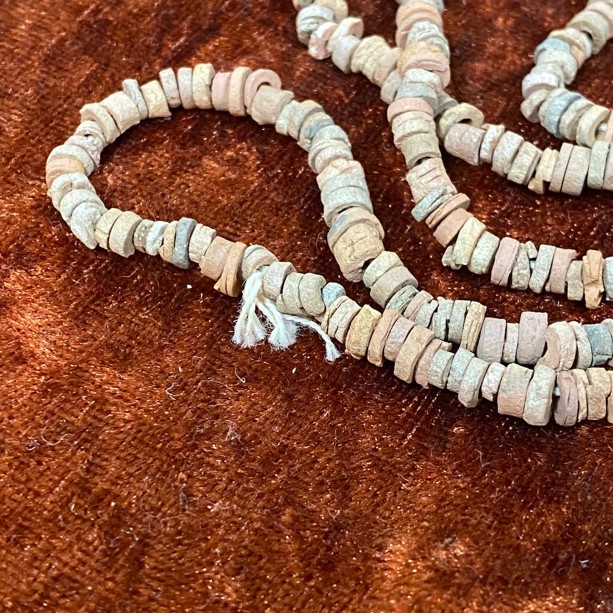 A close up photo of vintage faience beads showing the string, shapes and various colour tones on a brown background