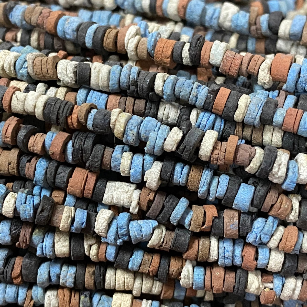 A strand of vintage faience clay beads in various shades of blue, black, cream, and brown, knotted on a string and arranged in lines