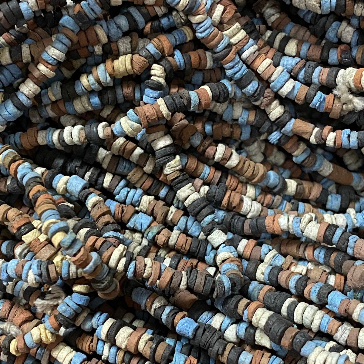 A collection of vintage faience clay beads in various shades of blue, black, cream, and brown, knotted on a string.