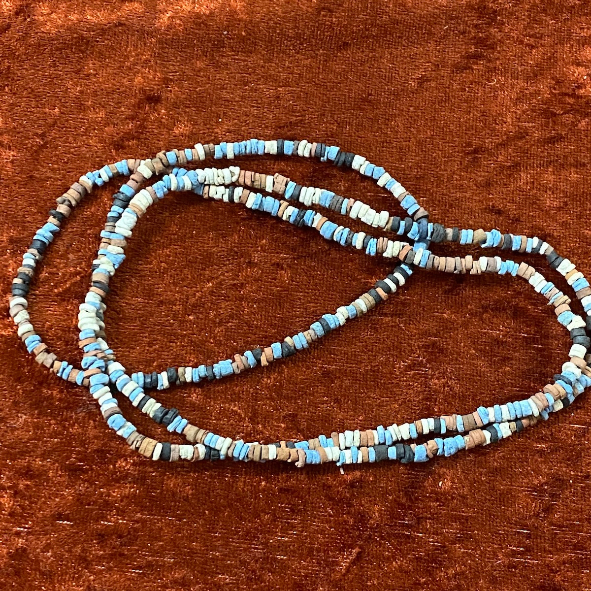 A strand of vintage faience clay beads in various shades of blue, black, cream, and brown, knotted on a string.