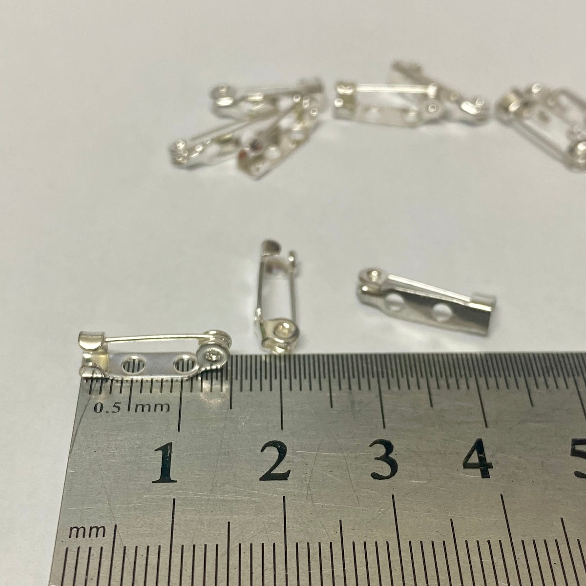 silver brooch backs displayed in a white dish with a metal ruler for scale
