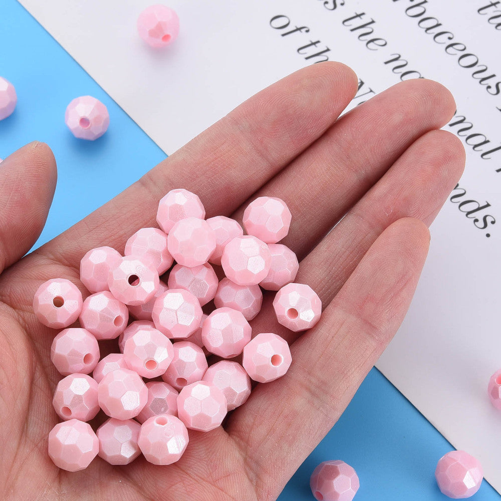 A hand holding a pile of small faceted light pink beads, with a few additional beads scattered on a blue and white background.