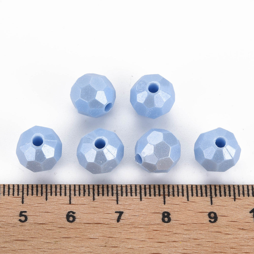 six faceted light blue beads arranged above a wooden ruler on a white background, showing their size relative to the measurement scale.