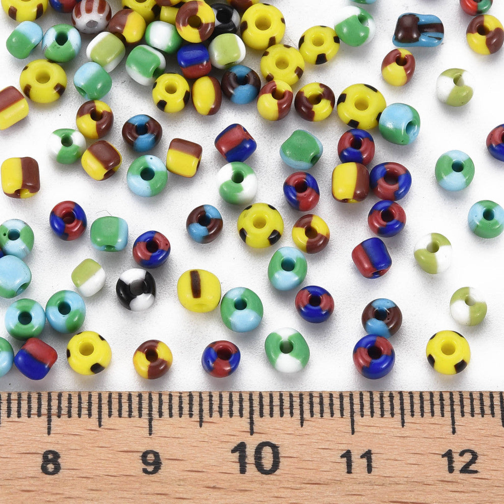 Assorted colorful glass seed beads with a wooden ruler for scale on a white background