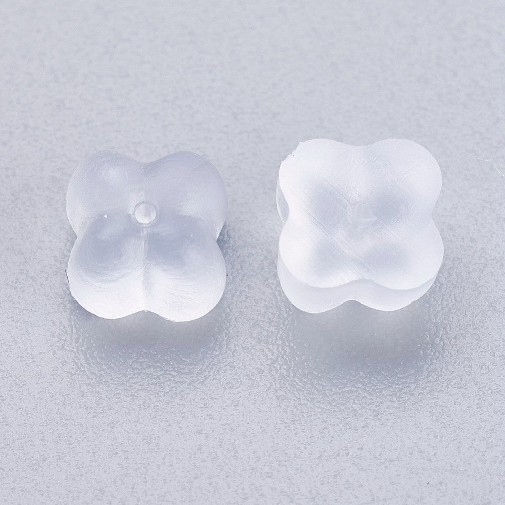 a pair of white silicone flower shaped ear stud back fittings on a grey textured background