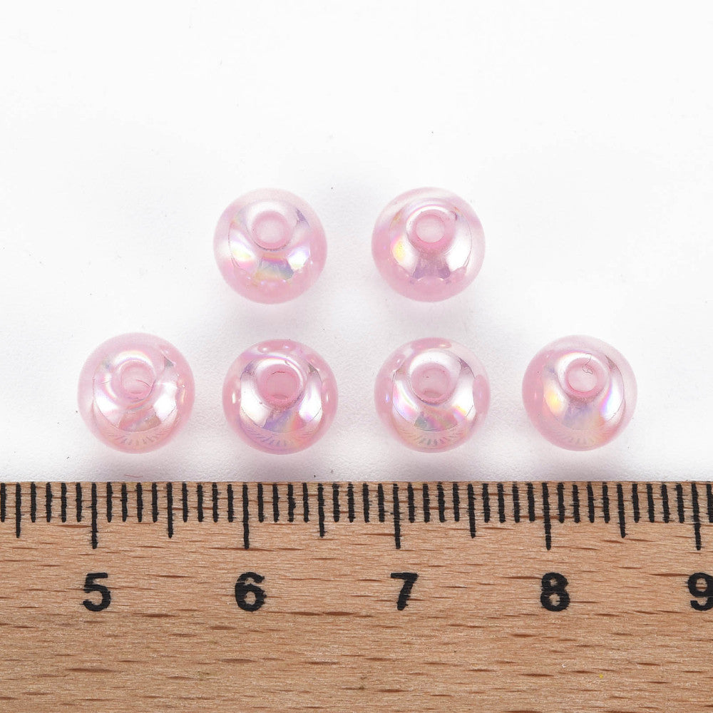 Six shiny pink pearl beads lined up on a wooden ruler for size reference.