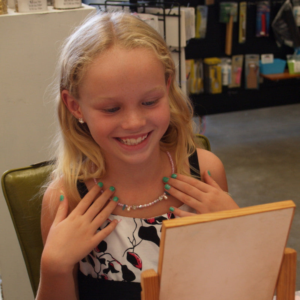 Girl proudly admiring herself in a mirror looking at the necklace she made at a workshop, with tool display in the background