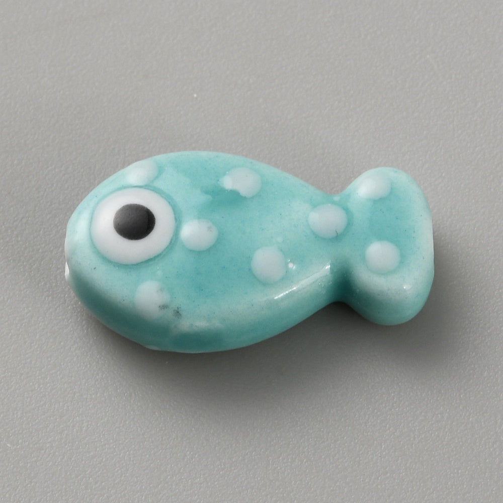 Turquoise fish-shaped bead with white spots and a black eye on a gray background