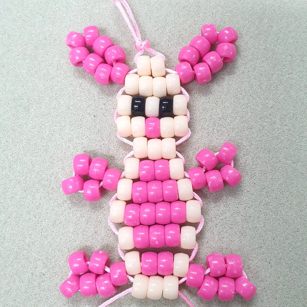 A completed lace-up kit depicting a pink and white rabbit made from pony beads and cord.