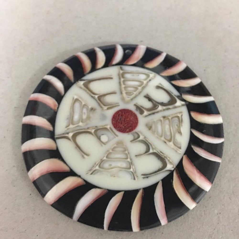 A circular pendant featuring layers of shell and resin in a geometric pattern with a smooth, shiny finish.