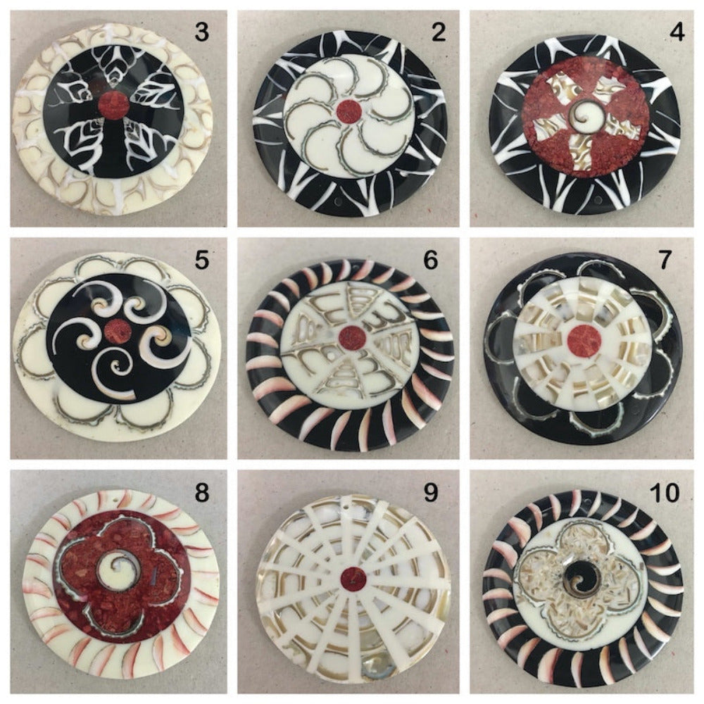 A collage of colorful shell and resin pendant with floral patterns, featuring a central shell design inlaid with resin, set against a black and white striped background.