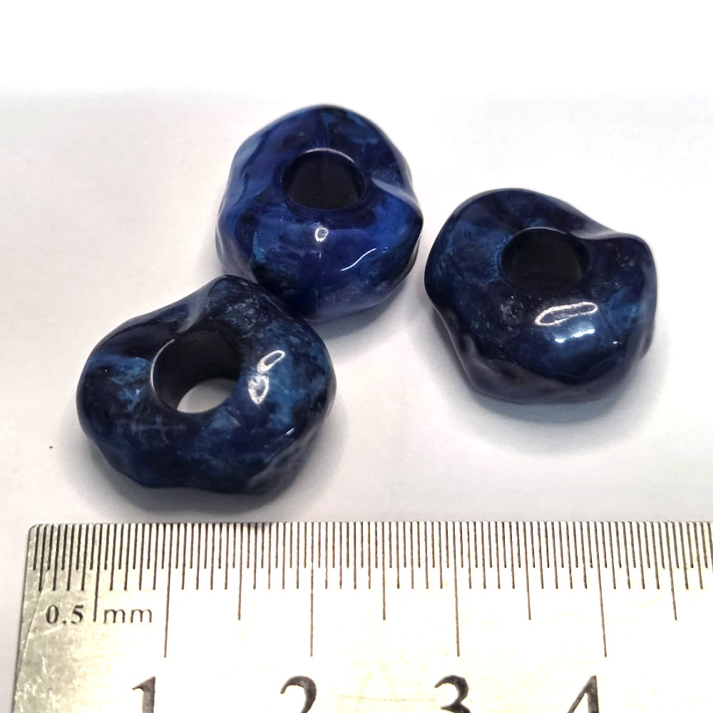 Three blue stone look beads with a ruler for scale on a white background