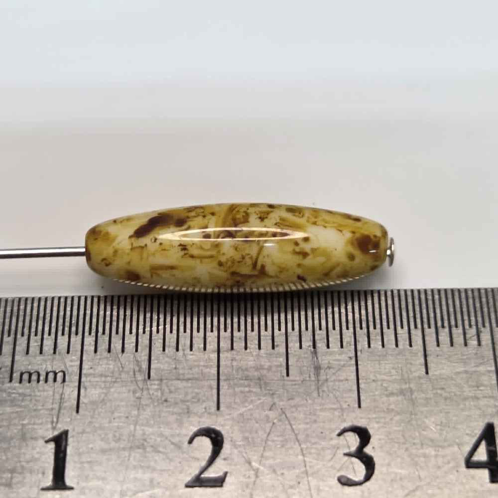 Close-up of a pile of brownish-golden cylindrical beads with dark spots on a ruler to show scale