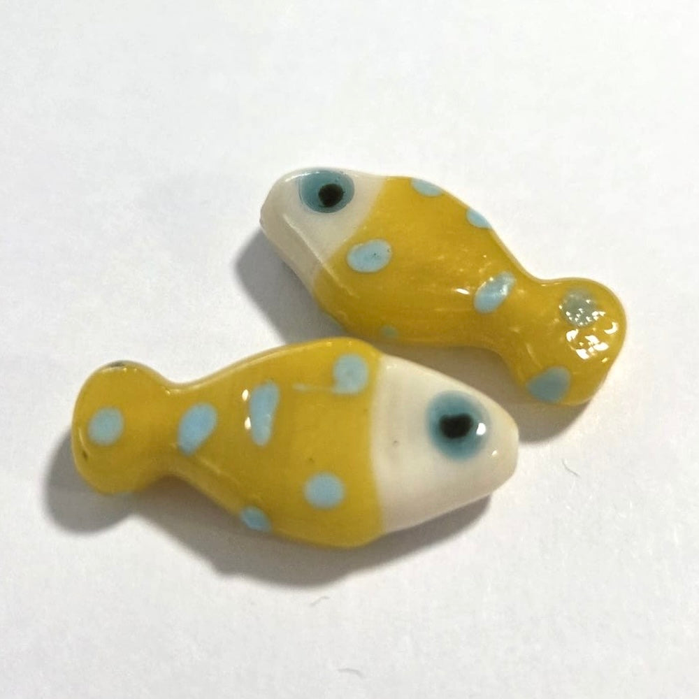 Two yellow fish-shaped beads with blue spots on a white background