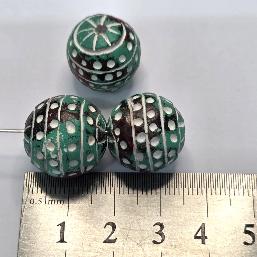 Three vintage clay green beads with white patterns on a white background, with a ruler for scale.