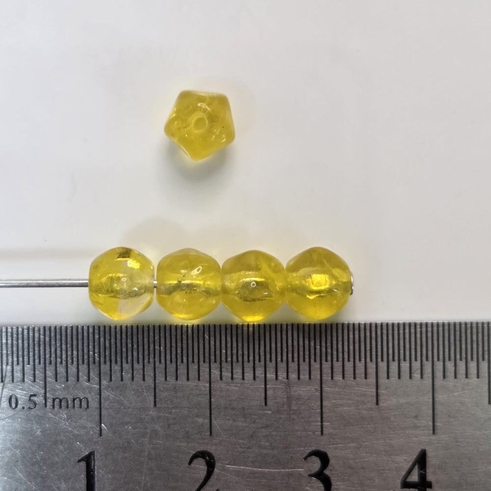Yellow beads and a pentagonal bead next to a ruler for size comparison on a white background