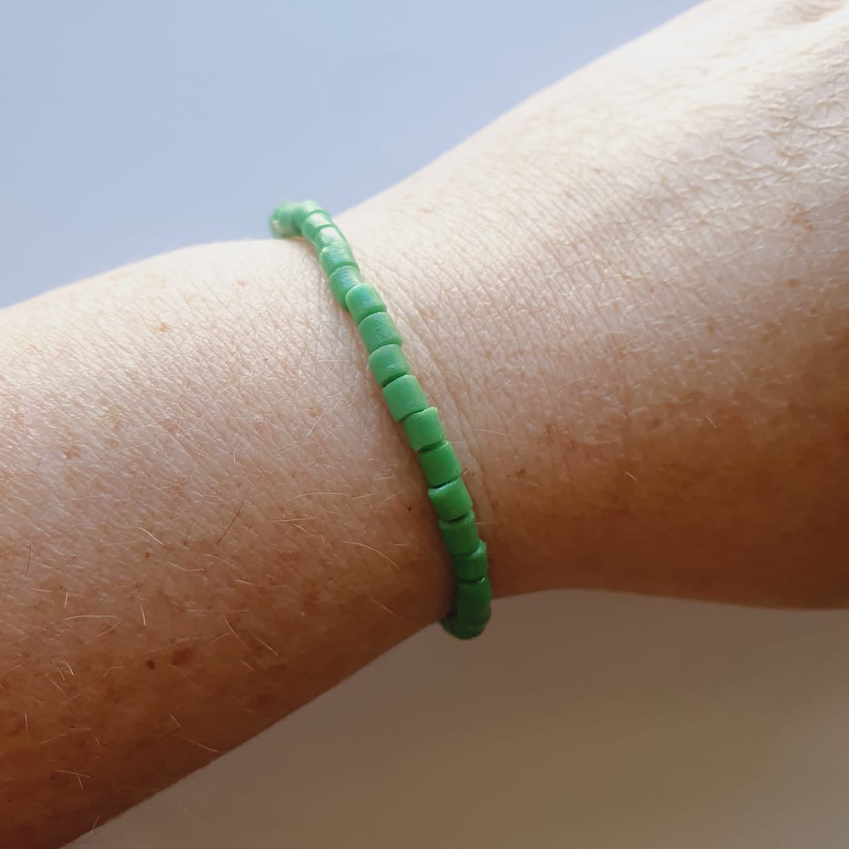 A bracelet on wrist showing vintage sand cast tube beads in green on a grey background