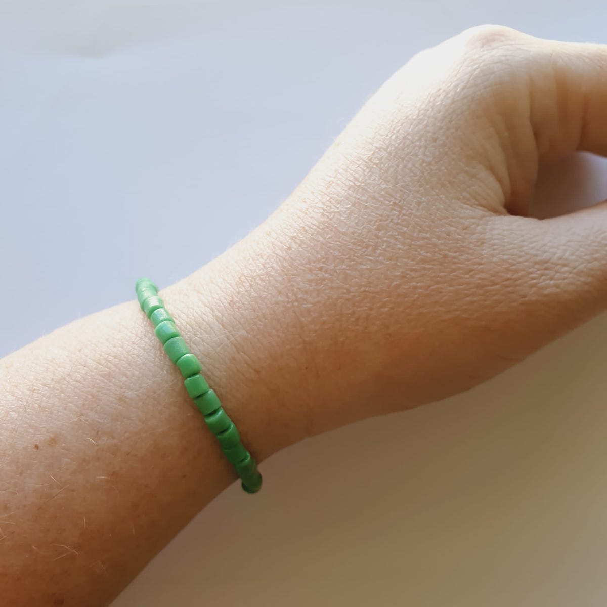 A bracelet on wrist showing vintage sand cast tube beads in green on a grey background