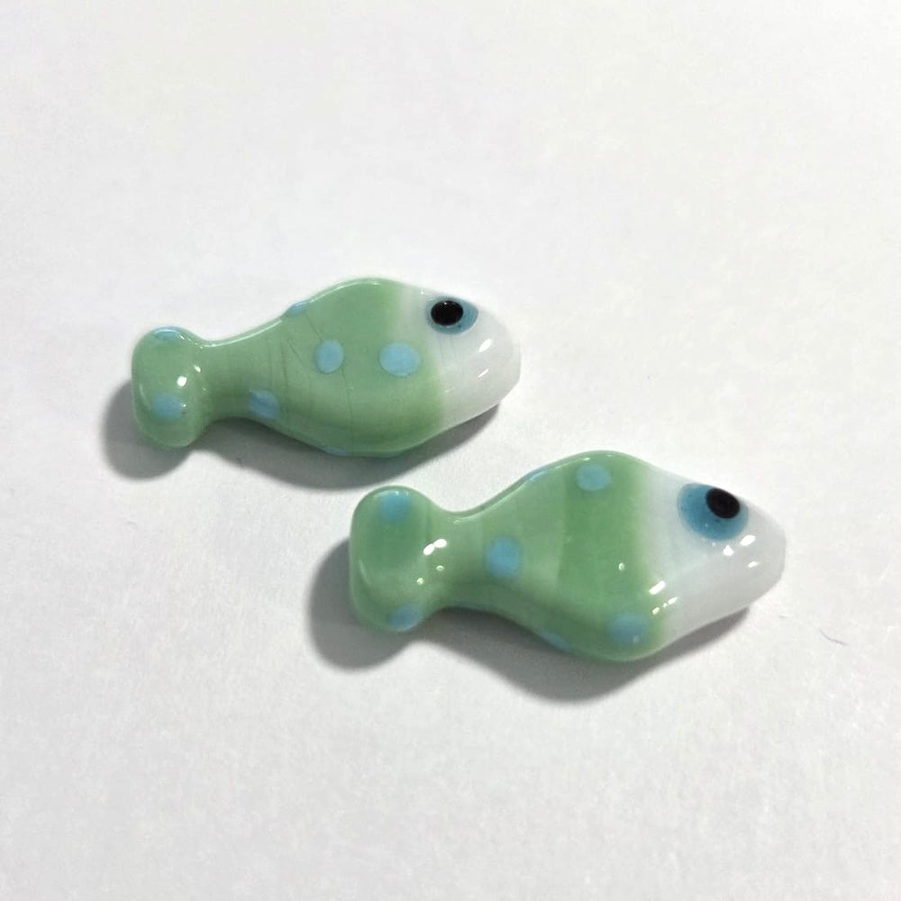 Two green fish-shaped beads with blue spots on a white background