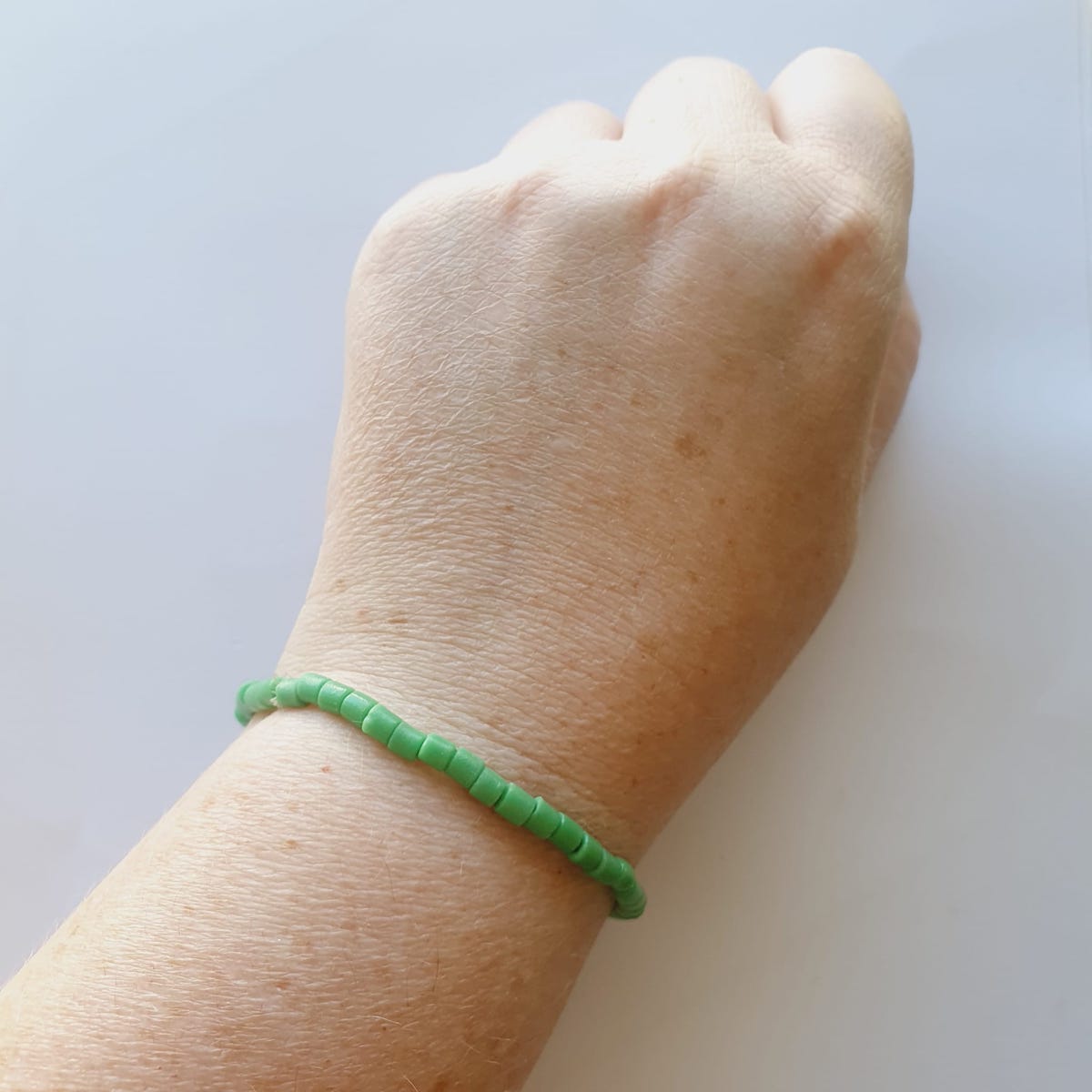 A bracelet on wrist showing vintage sand cast tube beads in green on a grey background
