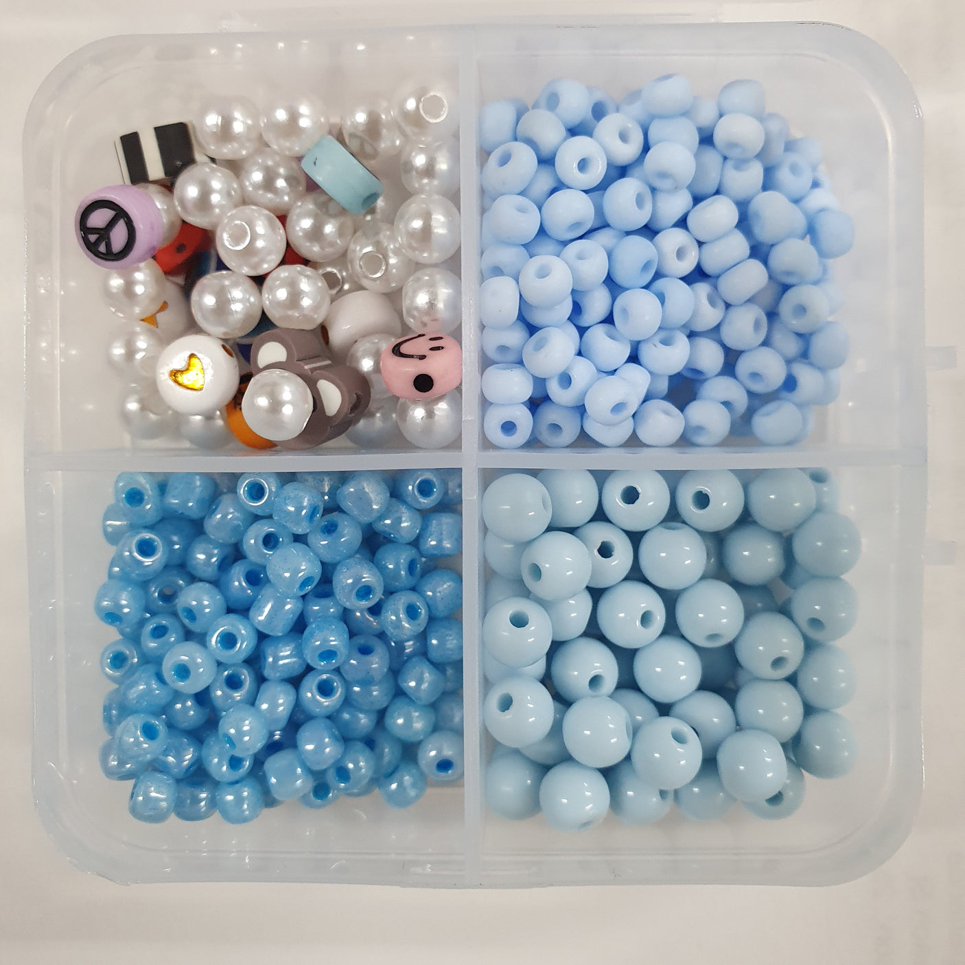 Clear plastic container with compartments filled with blue beads and decorative items on a light background