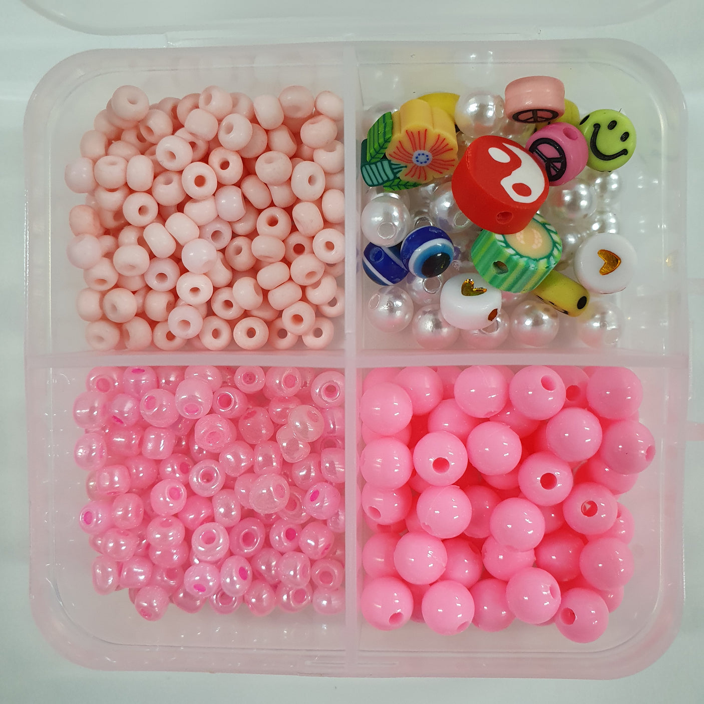 Assorted beads including pink, white, and multicolored in a clear plastic compartmentalized container.