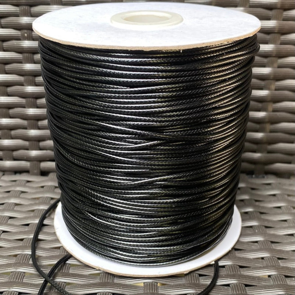 A spool of black waxed cord for crafting, displayed on a woven surface.