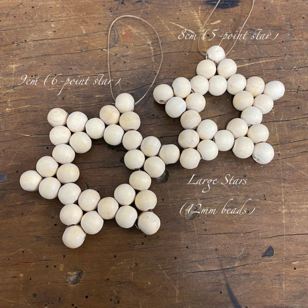 Two decorative stars with raw wood beads and camel-colored flat waxed cord woven together displayed on a wood surface