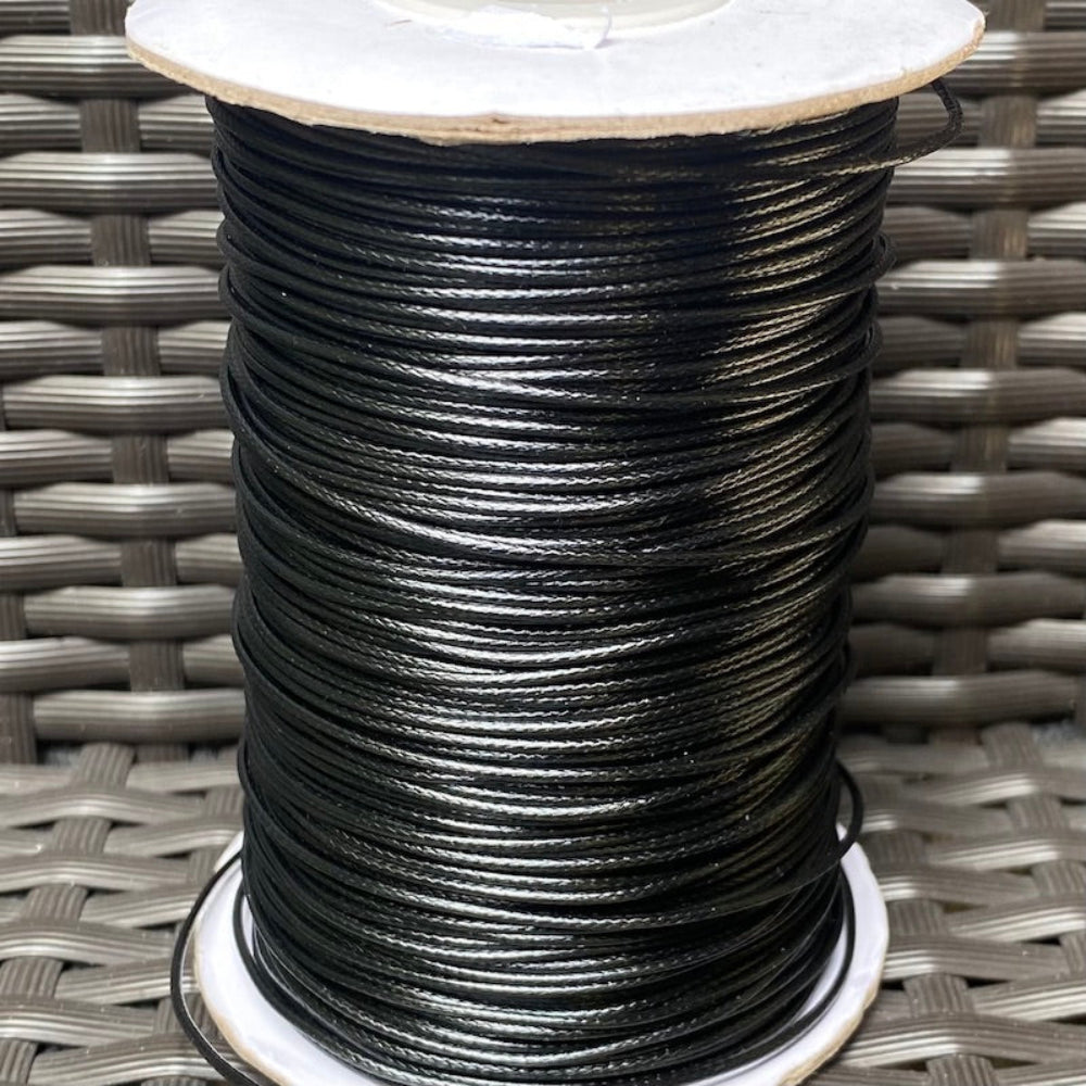 A spool of black waxed cord for crafting, displayed on a woven surface.