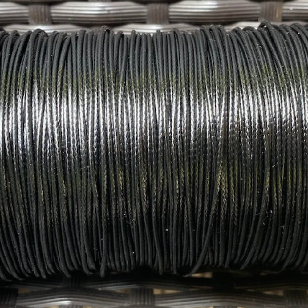 A spool of black waxed cord for crafting, displayed on a woven surface.