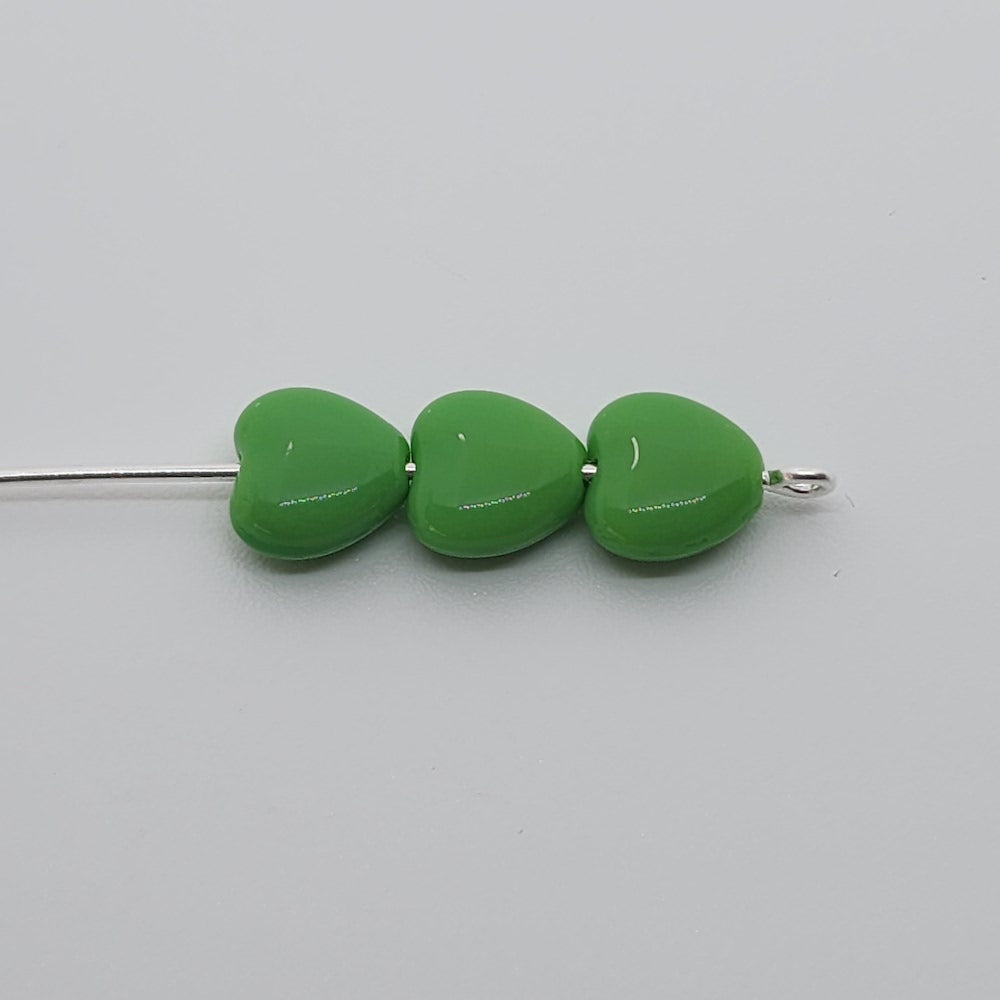 three green opaque heart beads threaded on a pin on a grey background