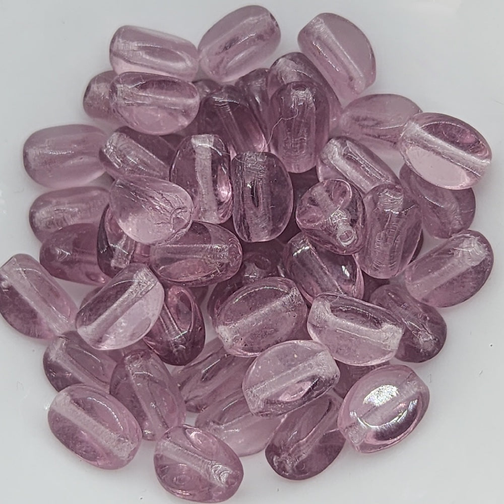 A close-up image of pinched rice-shaped Czech glass beads in a transparent light amethyst color.