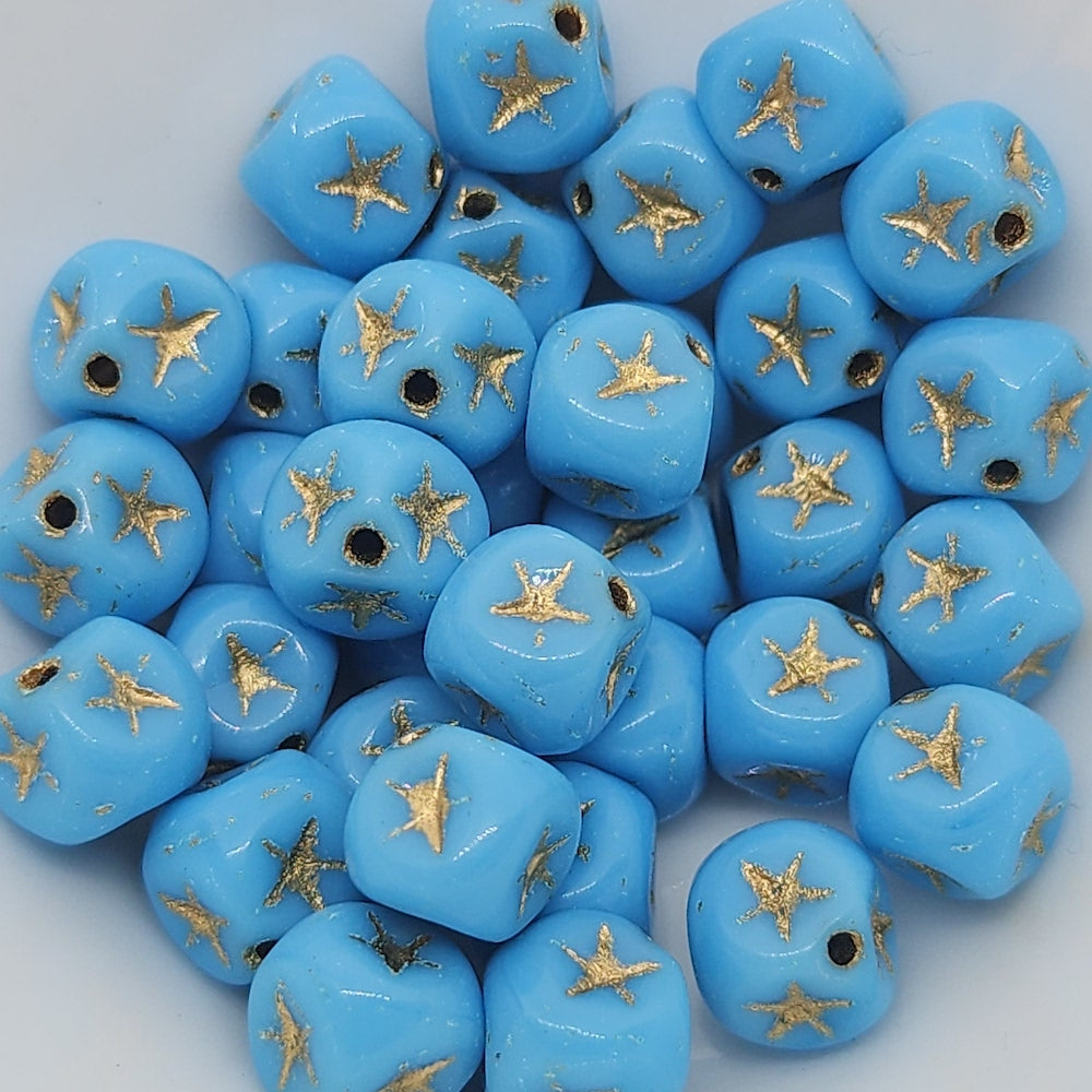 A collection of light blue cube-shaped beads with gold stars etched on them.