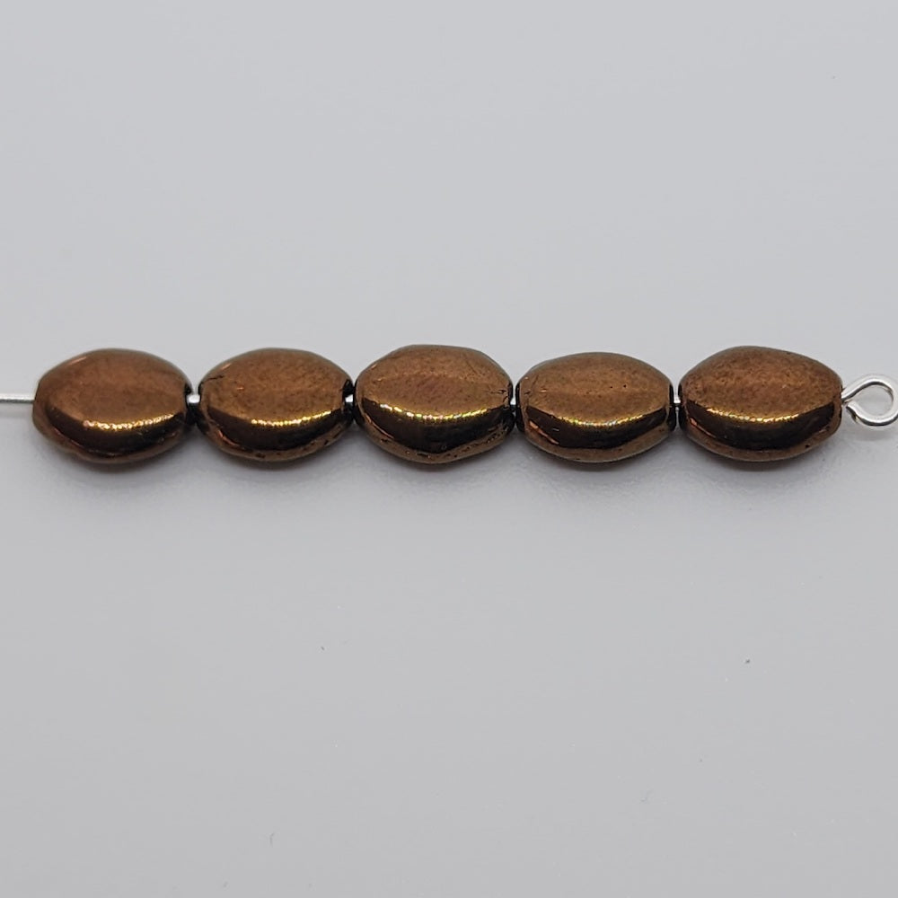 lustrous bronze oval flat beads on a pin on a grey surface