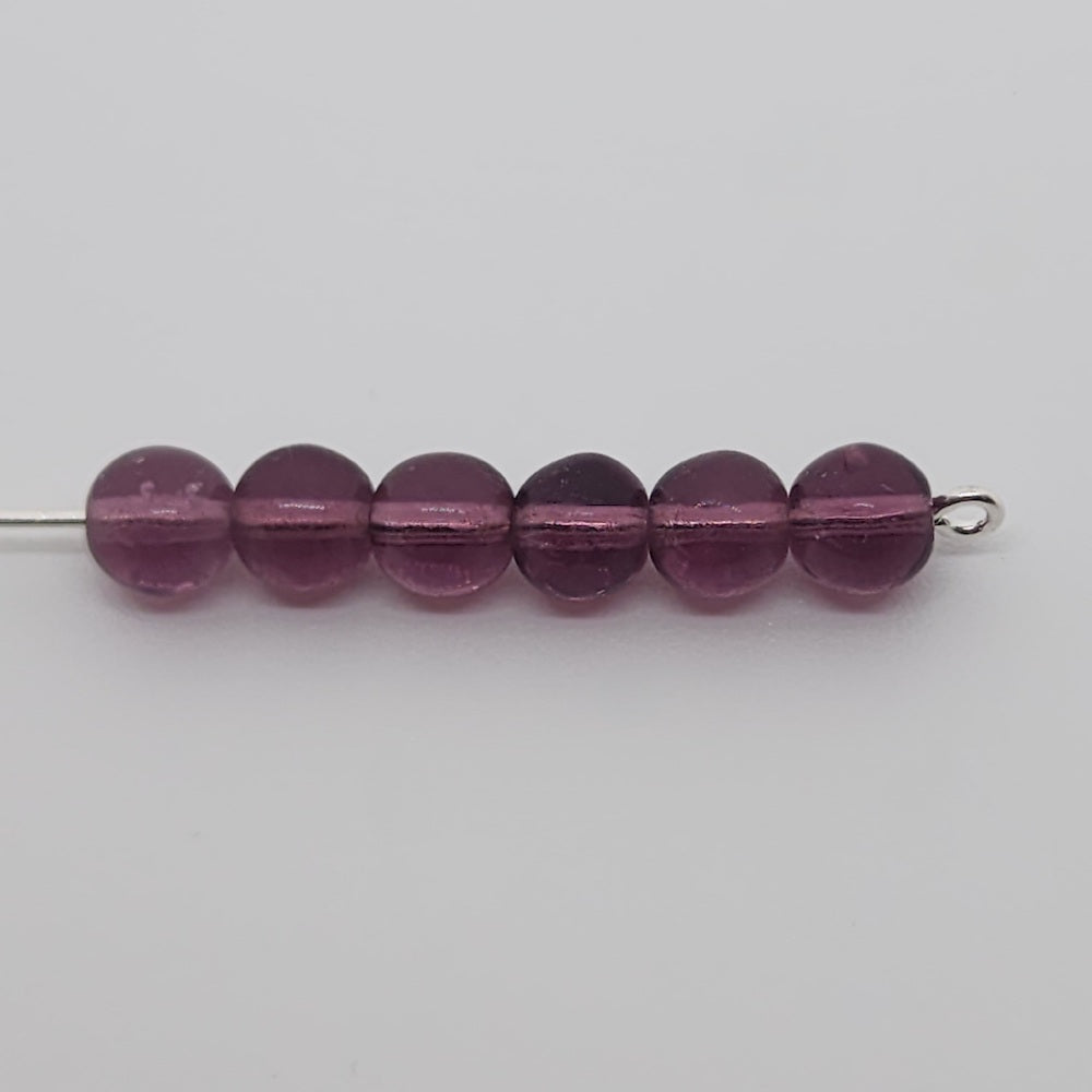 round purple glass beads on a pin on a grey background