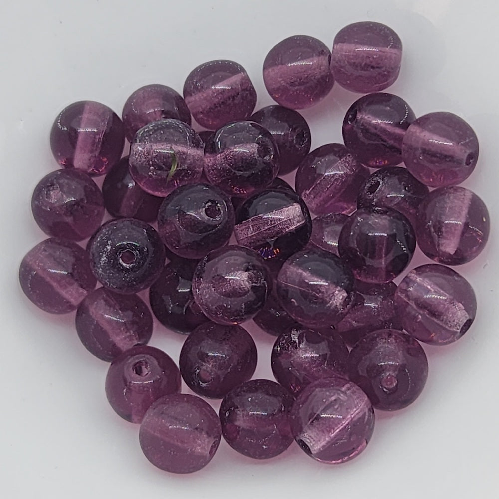 A collection of round, amethyst transparent Czech glass beads with a glossy finish, intended for crafting and jewelry making.