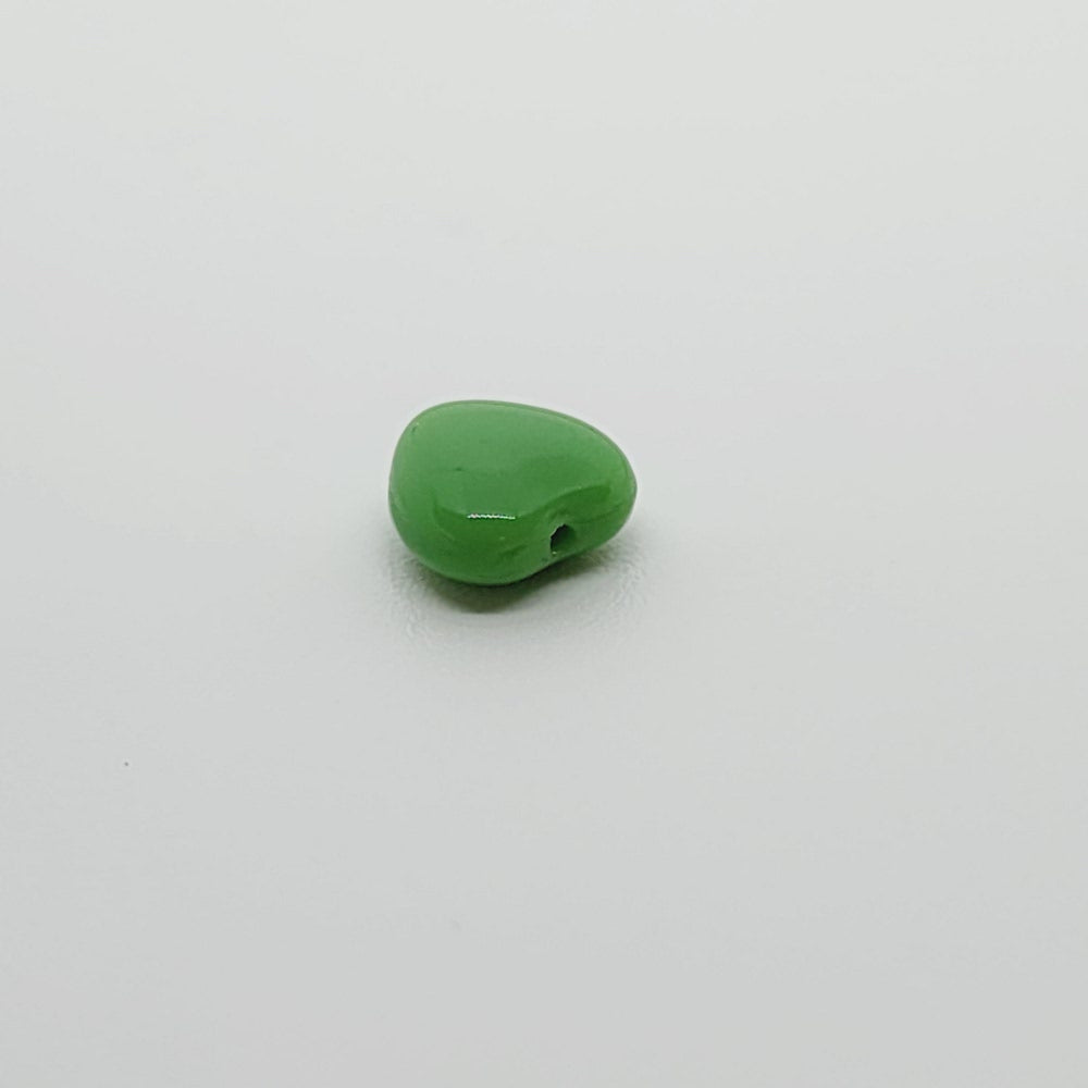 close up photo of one green opaque heart bead on a grey surface