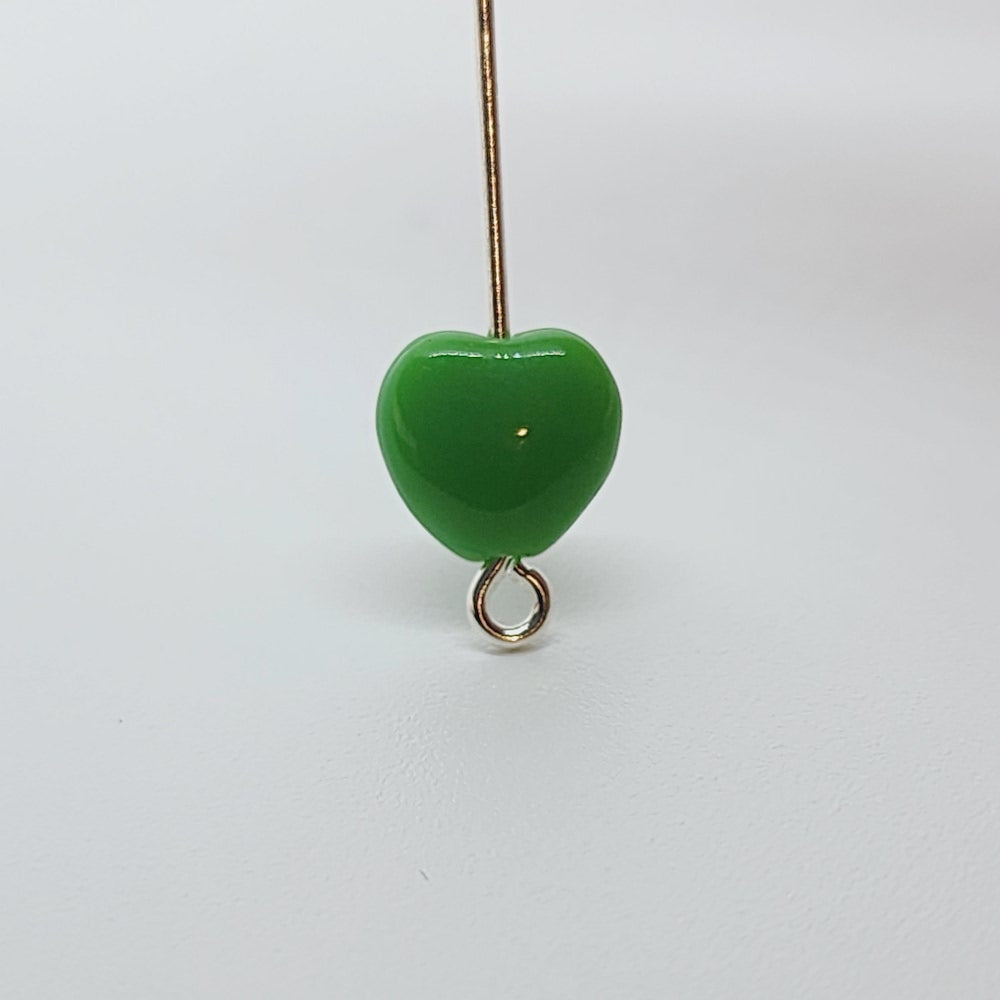 close up photo of one green opaque heart bead threaded on a pin to show direction of the threading hole
