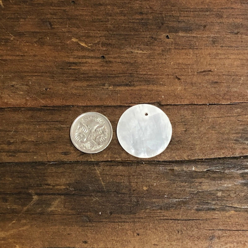 oyster shell disc with one pre drilled holesto use for making hanging decorations or craft projects on a wooden surface